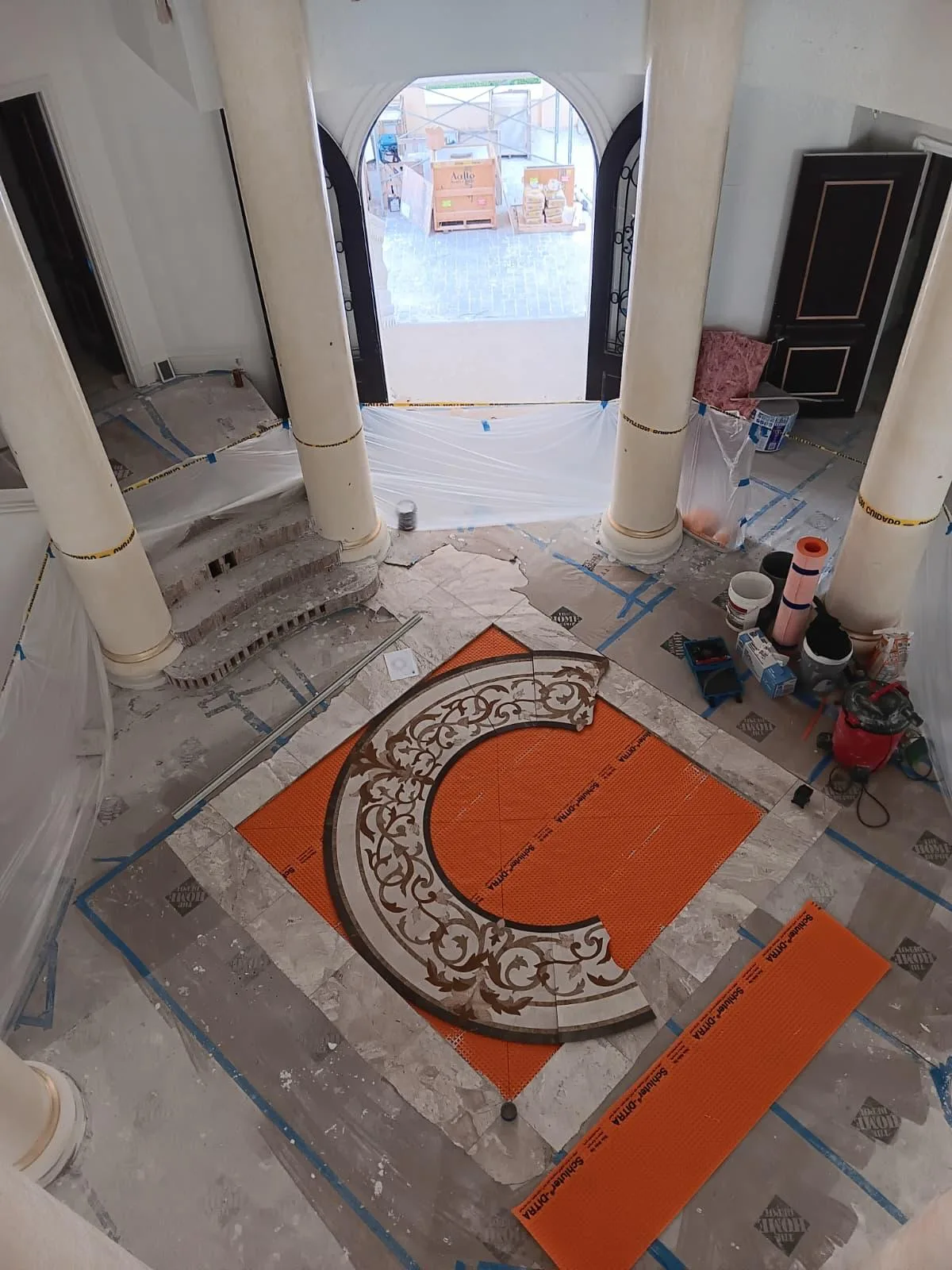 Round decorative mosaic medallion being installed on an orange membrane in an entry hall