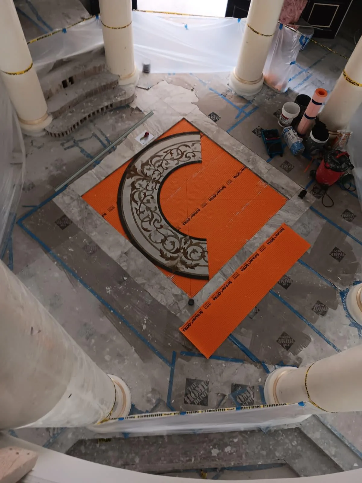 Round decorative mosaic medallion being installed on an orange membrane in an entry hall