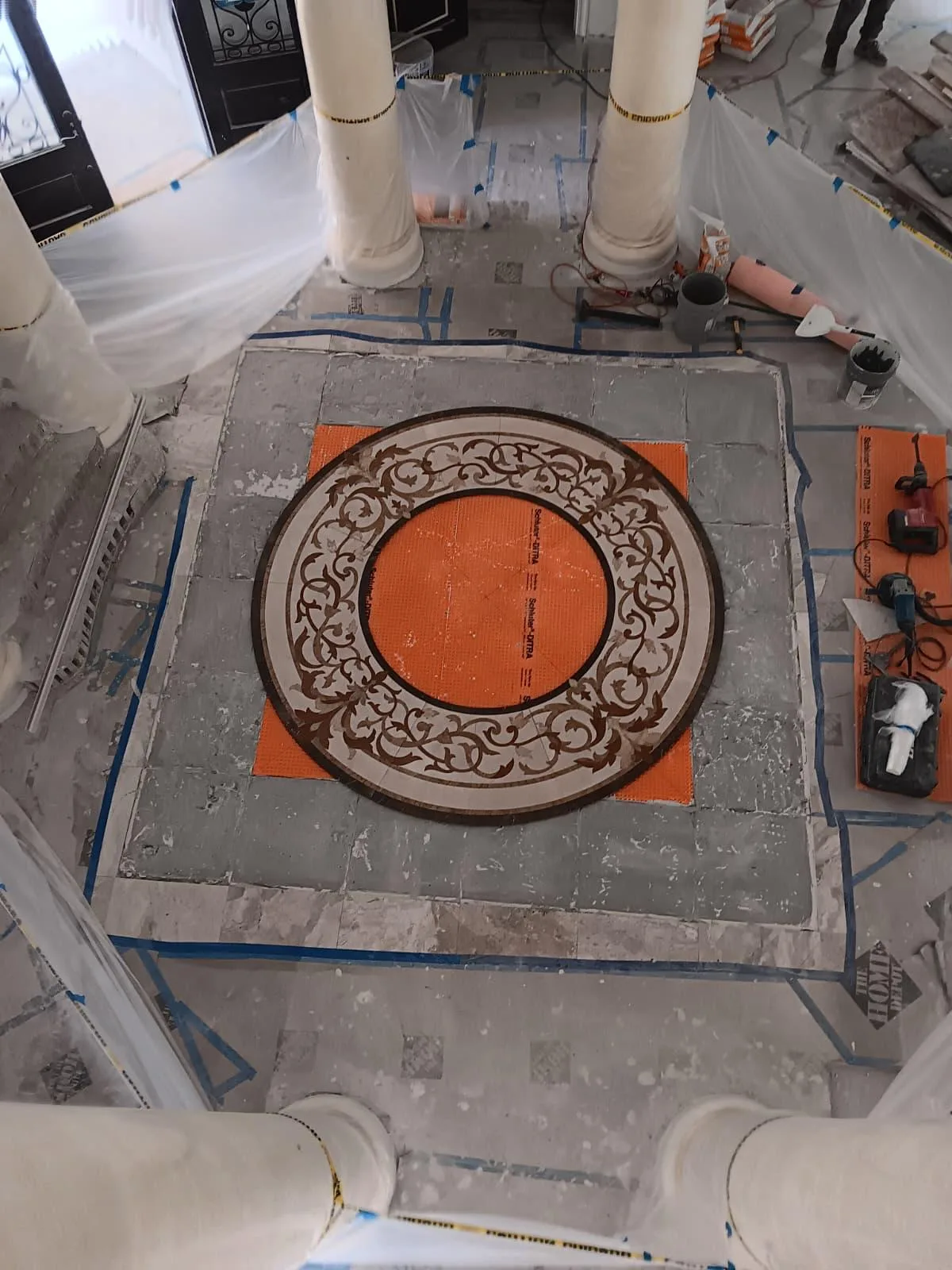 Round decorative mosaic medallion laid on an orange membrane in an entry hall