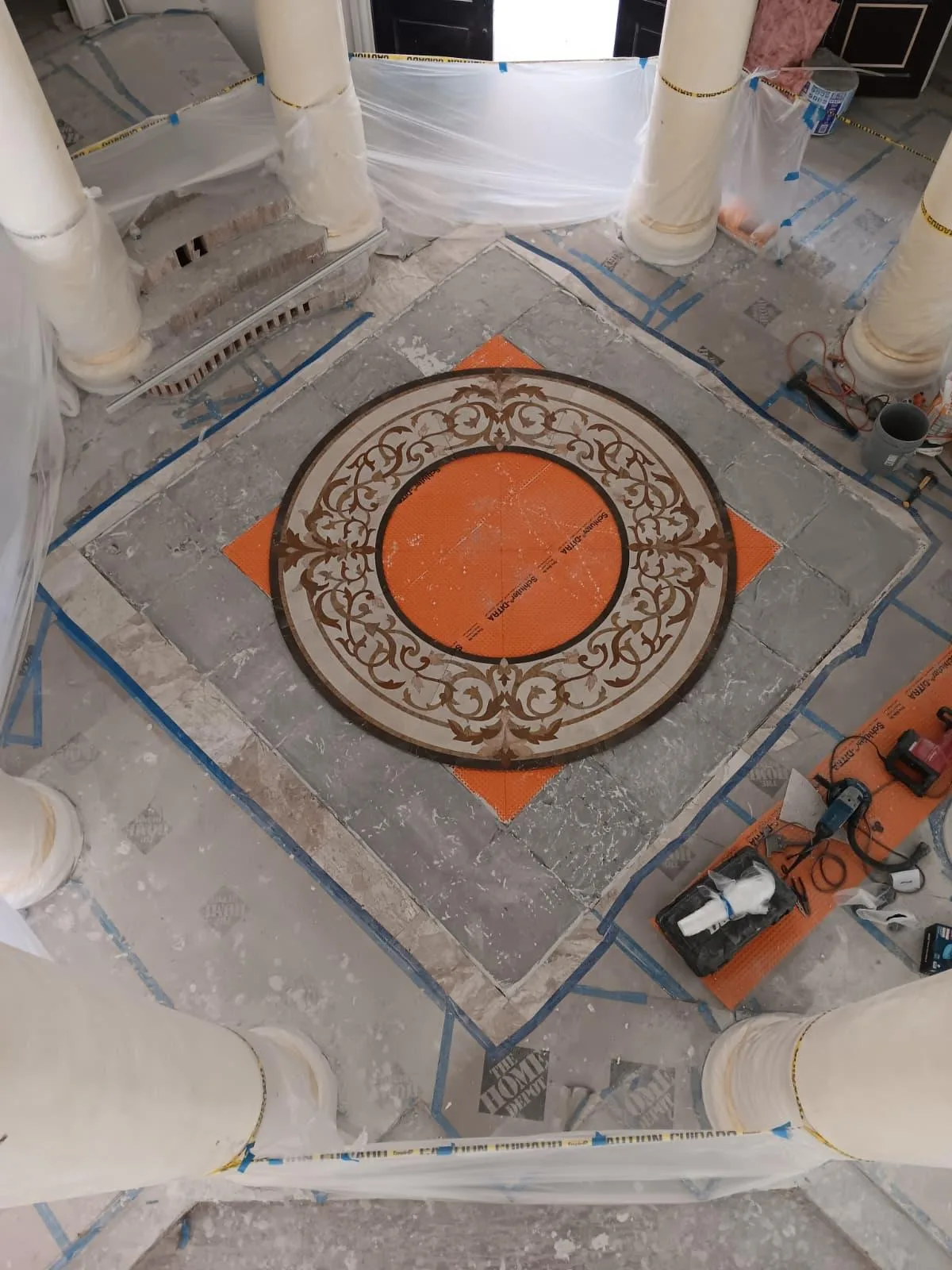 Round decorative mosaic medallion laid on an orange membrane in an entry hall