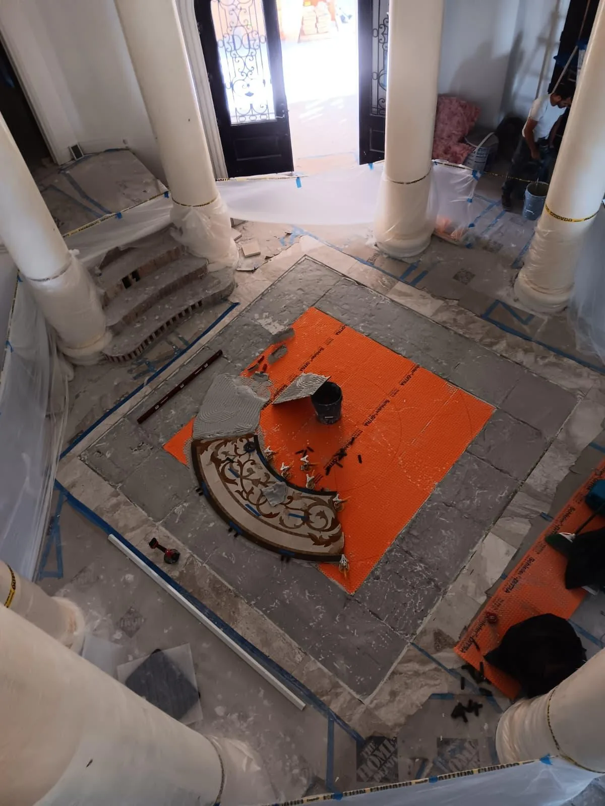 Round decorative mosaic medallion being installed on an orange membrane in an entry hall