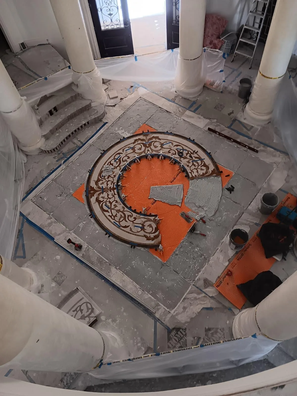 Round decorative mosaic medallion being installed on an orange membrane in an entry hall
