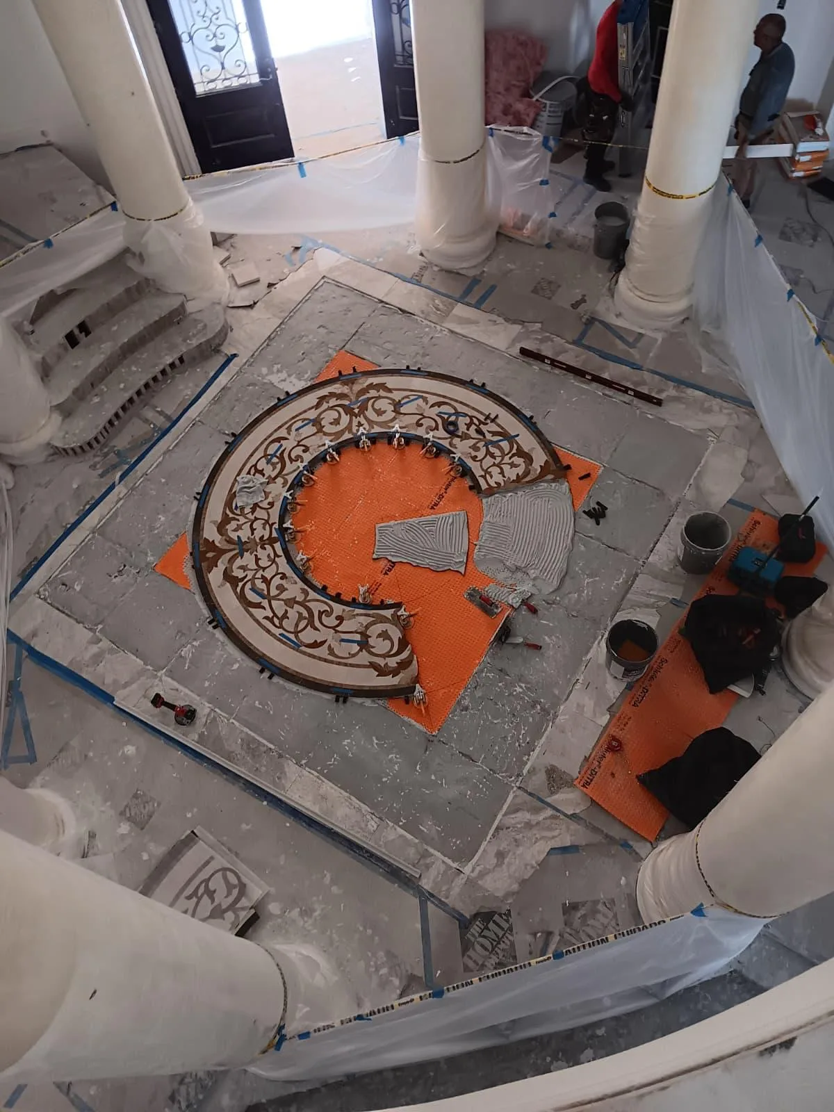 Round decorative mosaic medallion being installed on an orange membrane in an entry hall