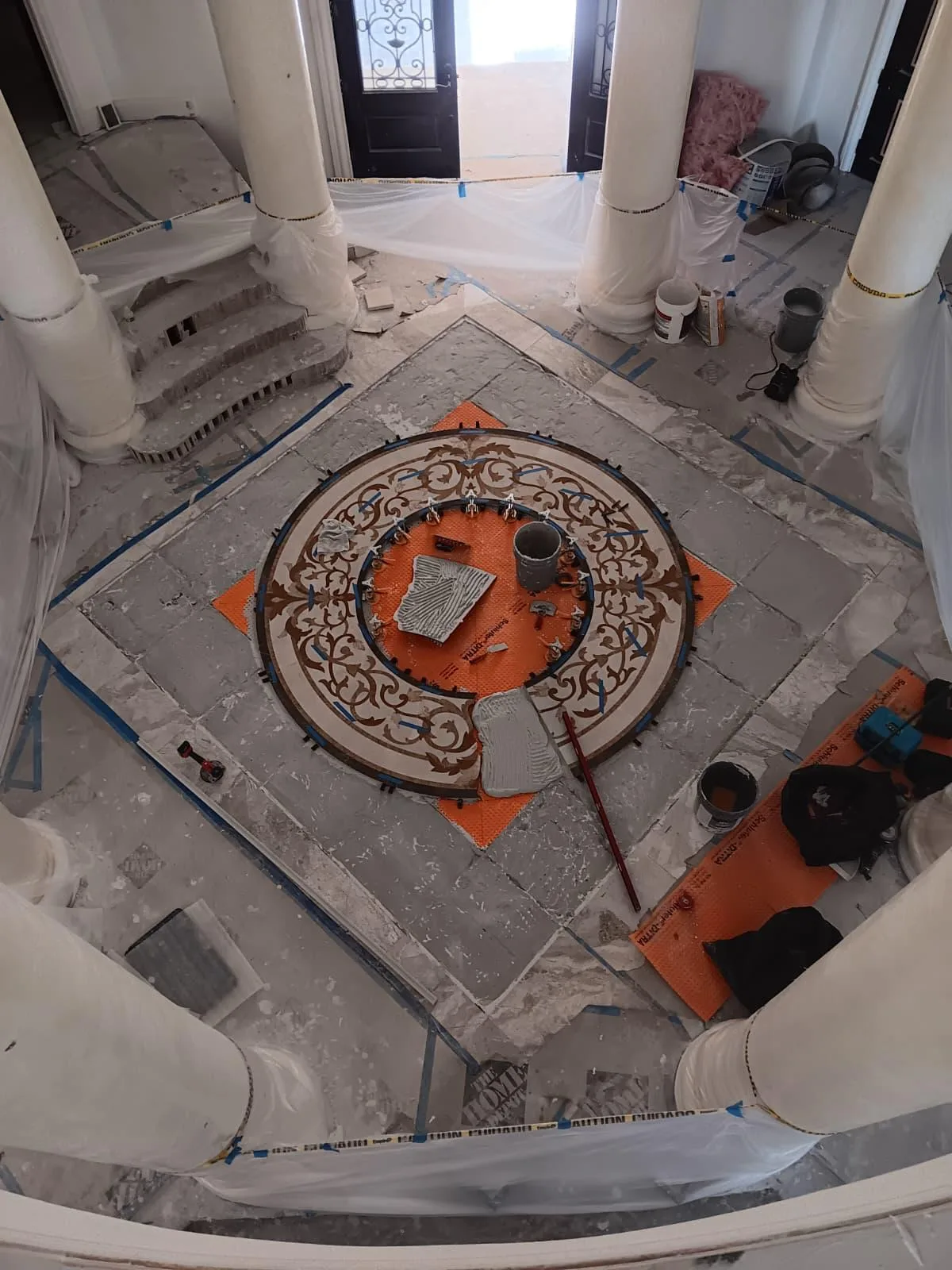 Round decorative mosaic medallion being installed on an orange membrane in an entry hall