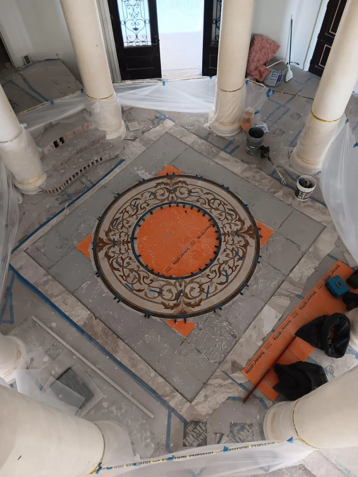 Round decorative mosaic medallion laid on an orange membrane in an entry hall